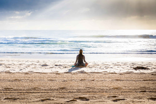 A woman sitting in quiet meditation facing the ocean, symbolizing the calm and intention-setting explored in Sol Aromatics' Manifestation Workshop: Connect Scent to Intention
